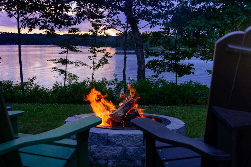 Two chairs sit next to a fireplace with the water behind.