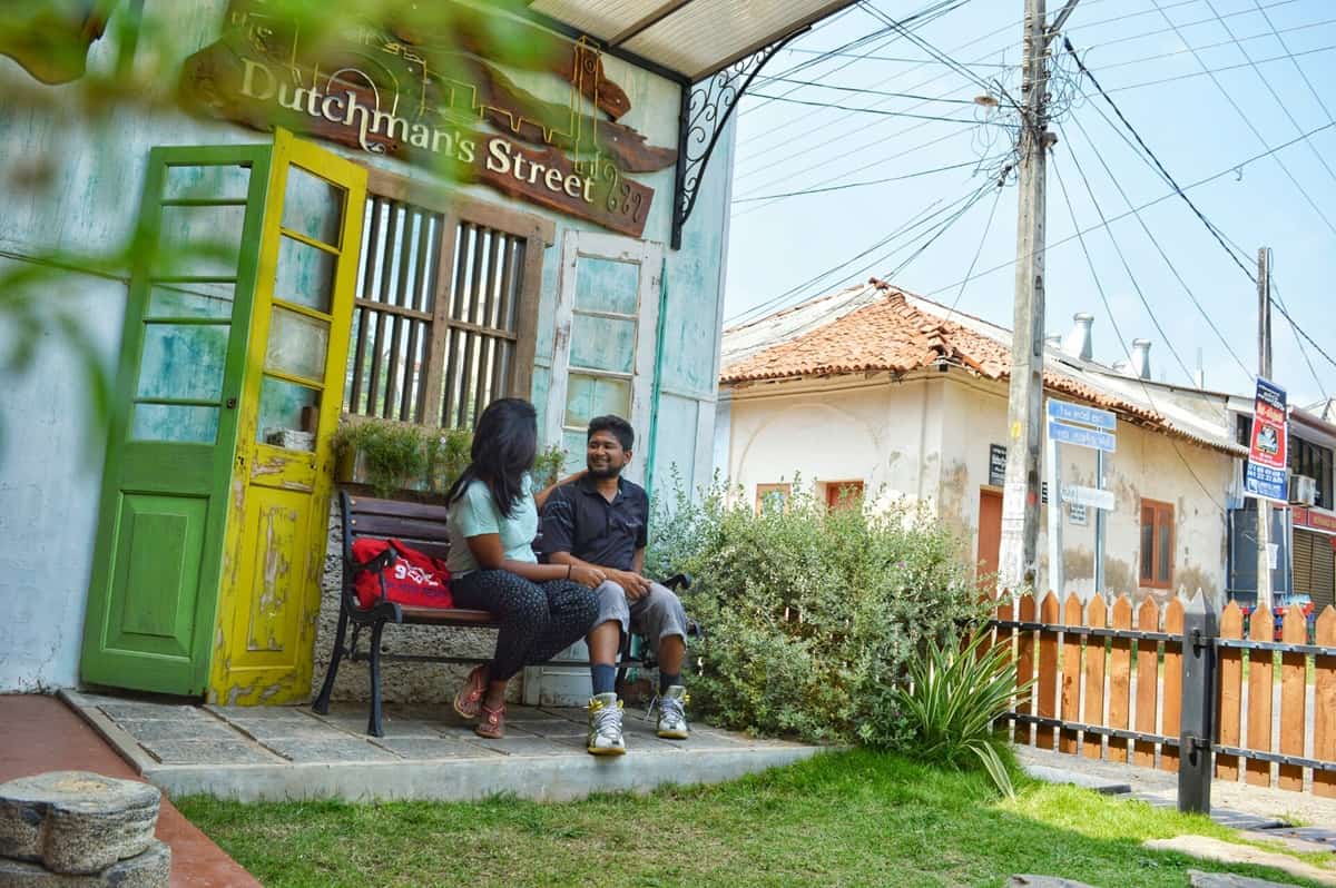 A couple sits on a bench in front of a blue building