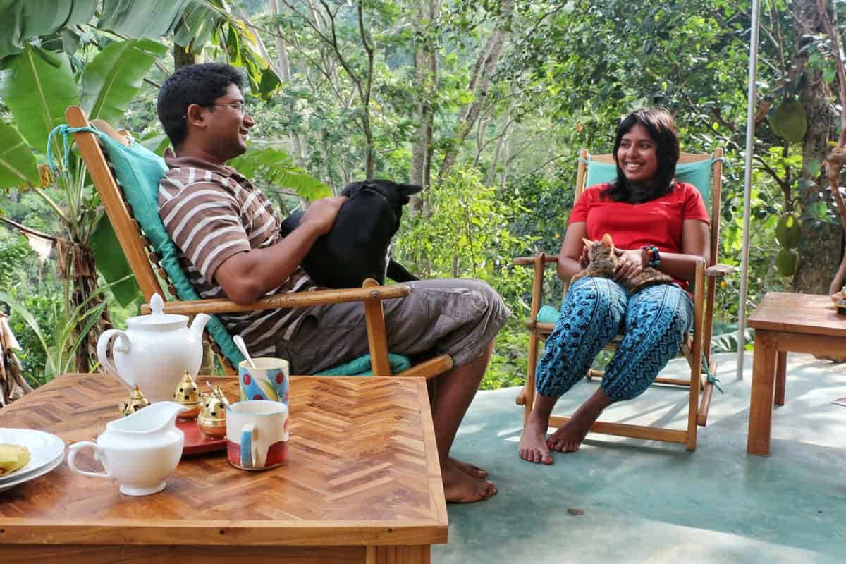 A couple sits outdoors in chairs. The man holds a pet.