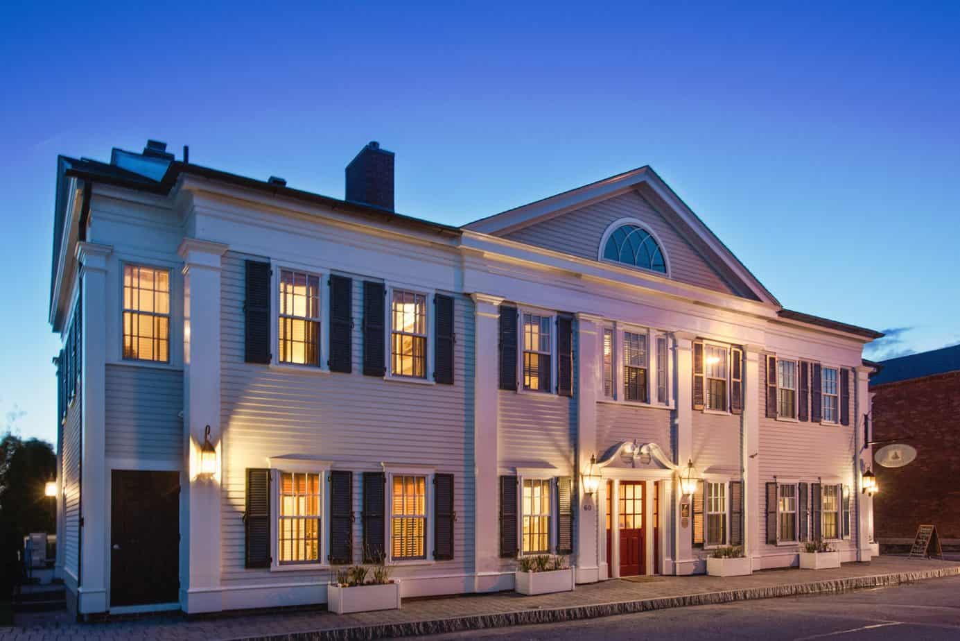 A big white building with black shutters under a blue sky at night.