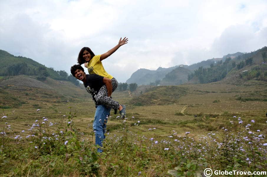 A man holding a woman on his back while making a funny face in an outdoor green landscape.