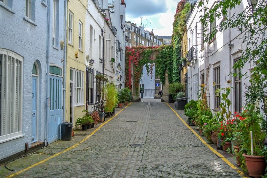 A small cobblestone street with colorful buildings on either side with colorful vines hanging from a few of the buildings. 