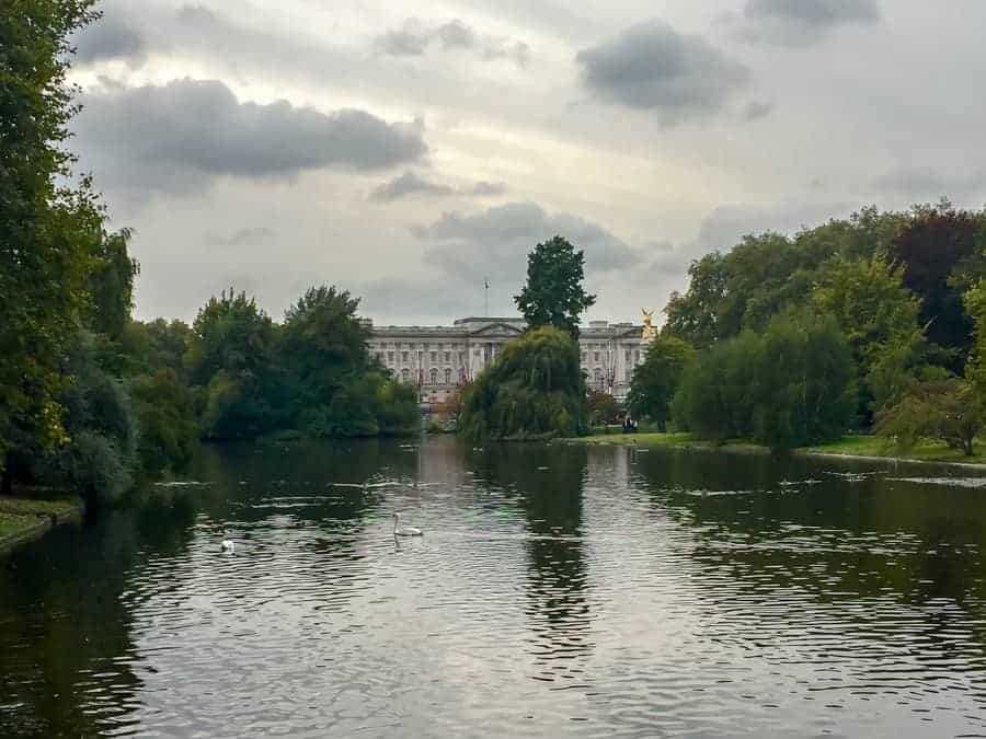 A small pond surrounded by trees leading to a large government building. 