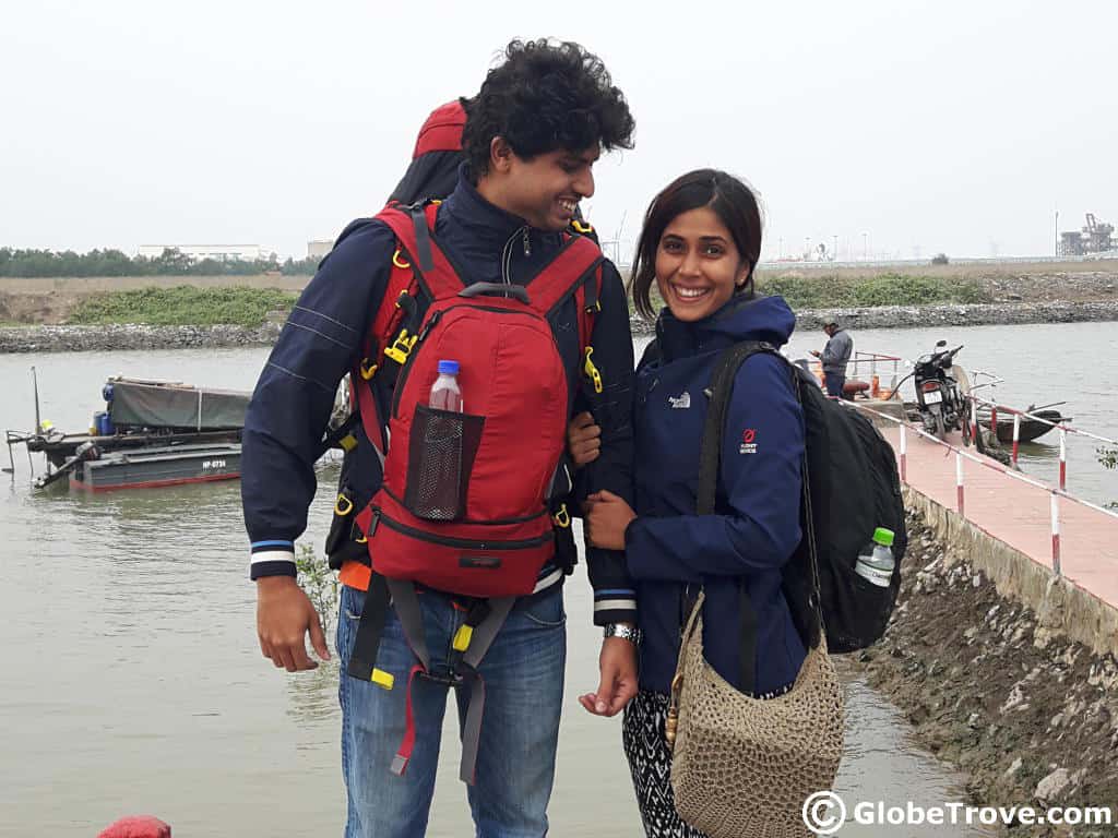 Man and woman smiling outdoors next to the water.