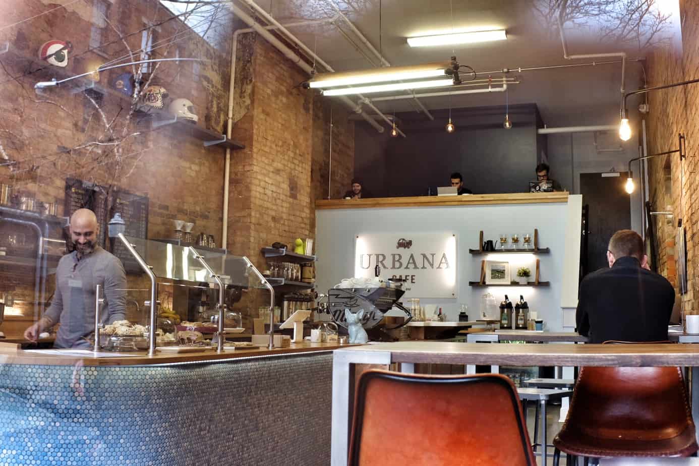 A man working behind a counter at a cafe. Other people sit at the cafe tables, working.