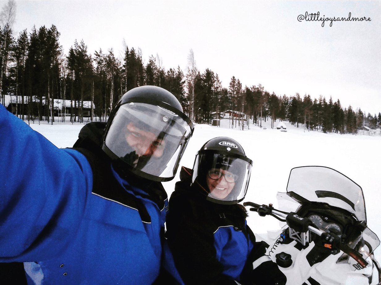 A couple sitting on a snowmobile outdoors in the snow.