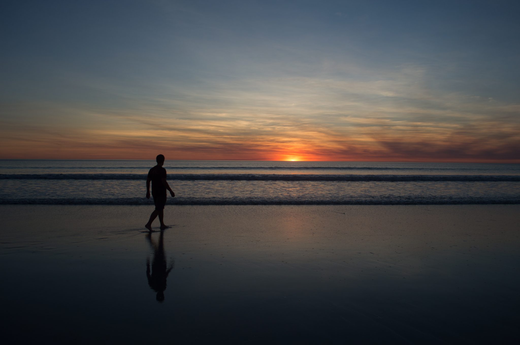 A man walks along the beach as the sun sets