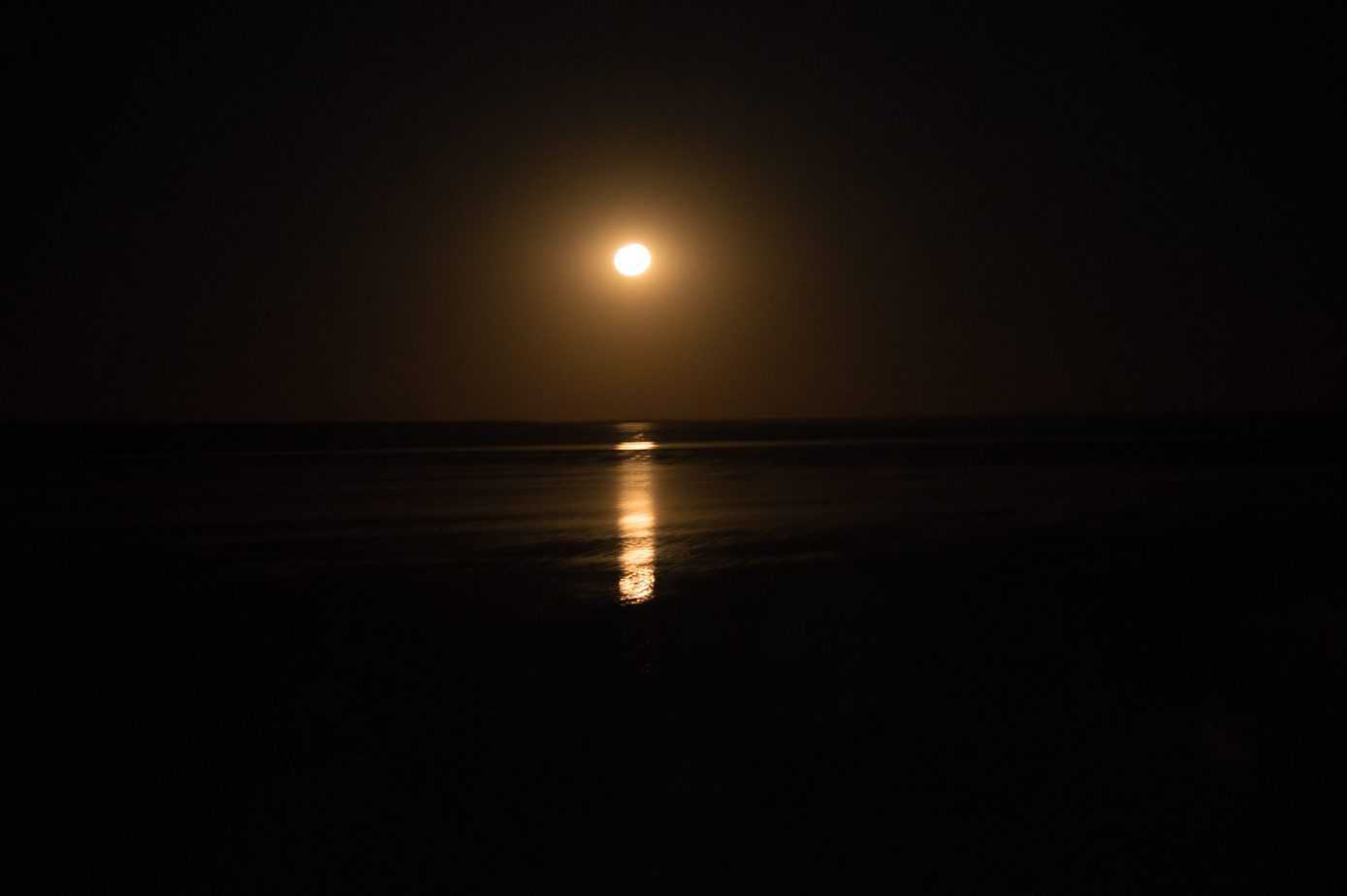 The bright moon is in the sky over the ocean.