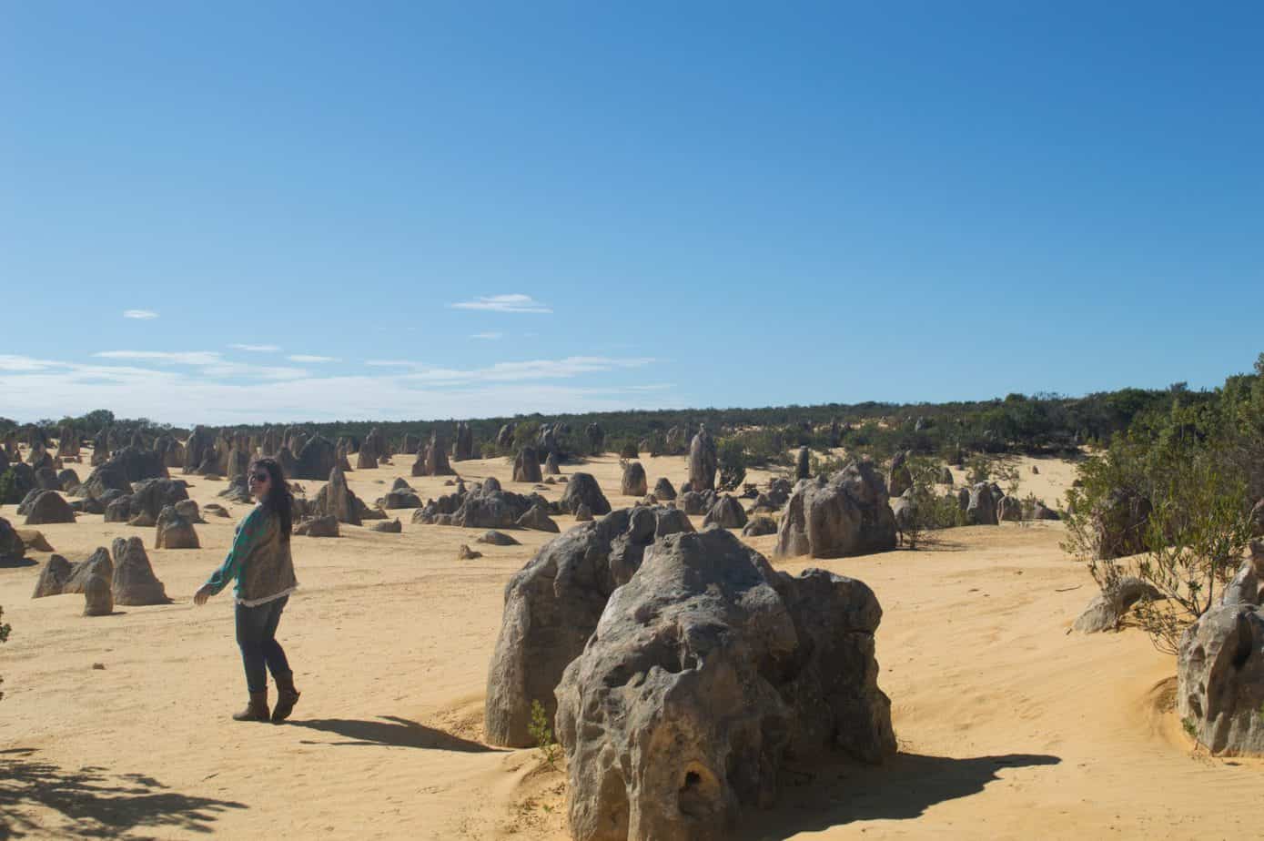 A woman walks around a sandy area with big rocks