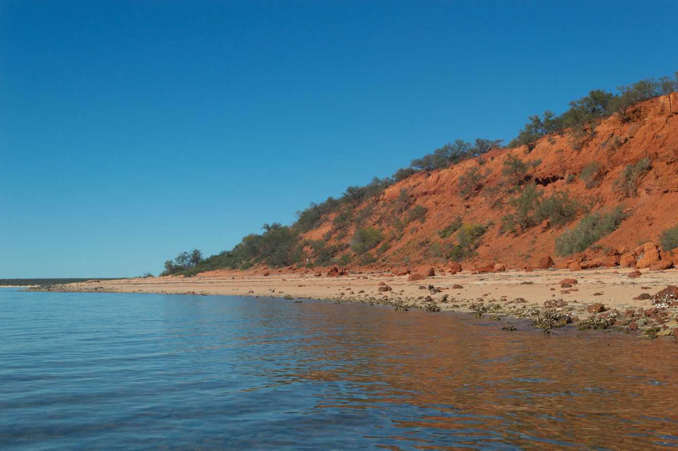 A calm body of water is next to a red cliffside