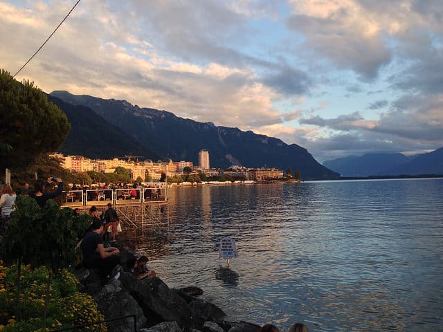 People relaxing on rocks near the ocean. Mountains are in the background.