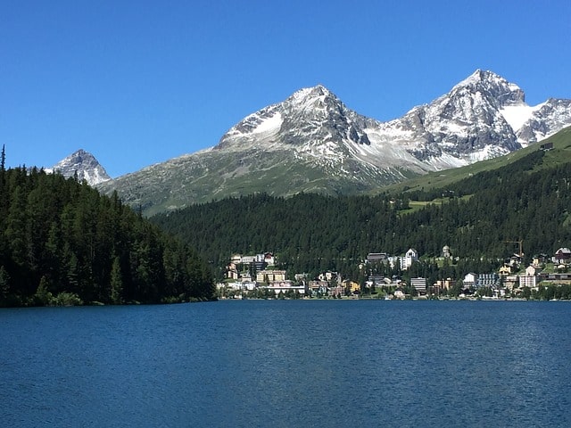 A town sits on the opposite side of the ocean. Big snowy mountains are behind.