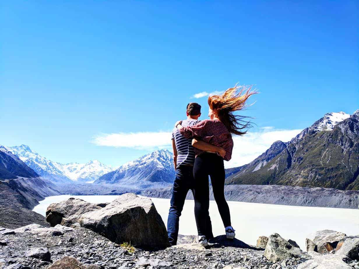 A couple hugs each other and looks out to the mountains.