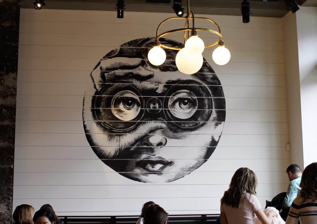 Group of people in a cafe with a black and white art piece on the wall.