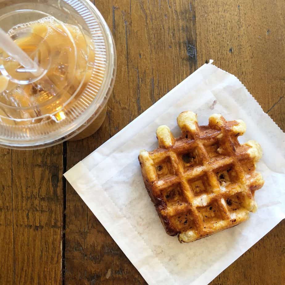 Waffle and a cup of iced coffee on a wooden table.