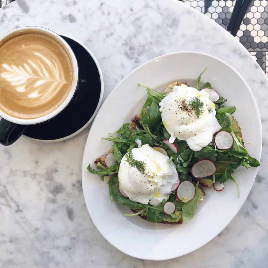 Photo of avocado toast with eggs next to a coffee.