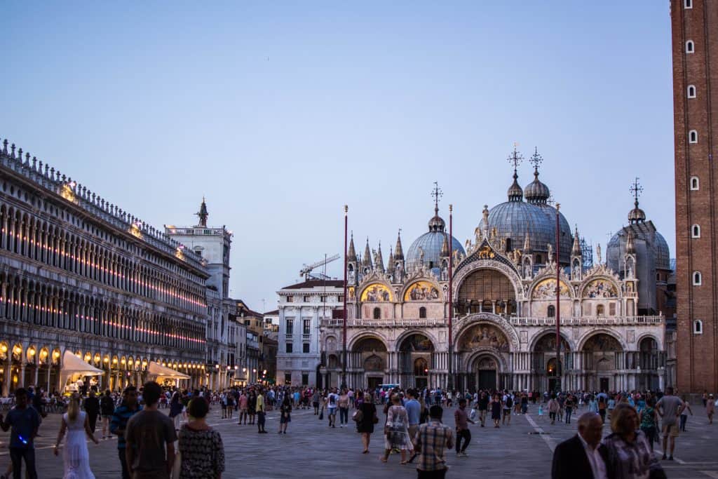 People walking around a plaza with a big church behind.