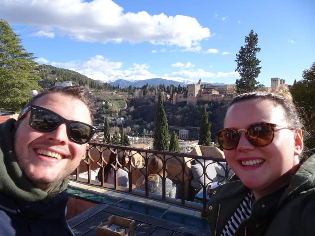 A couple smiles with a view of a city behind them.