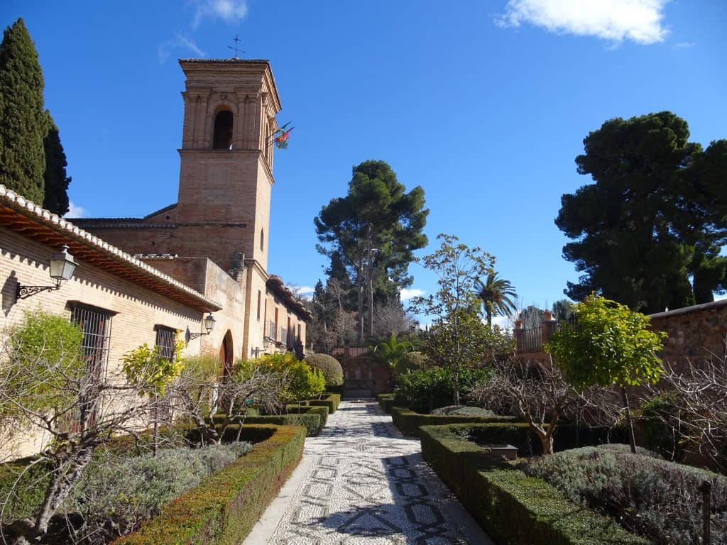 An empty garden lined with unique shrubs. A tall building stands on the left.