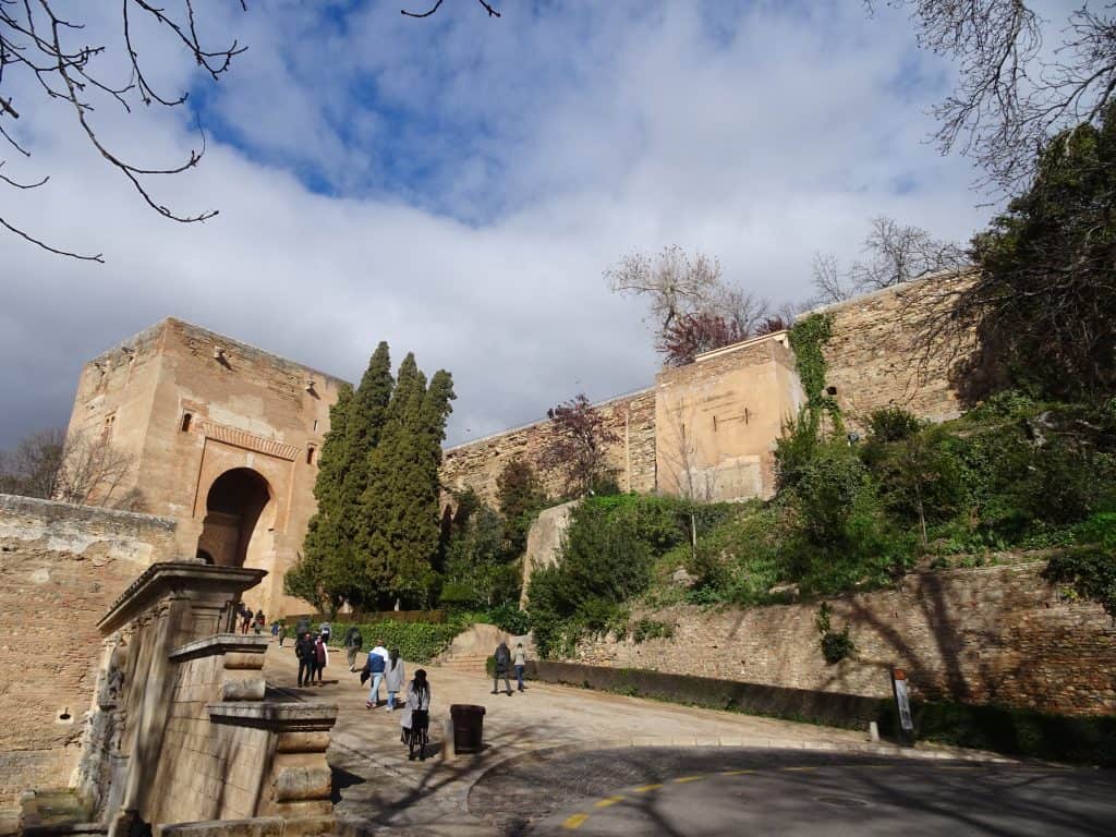 People walk around a walkway next to a tall fort.