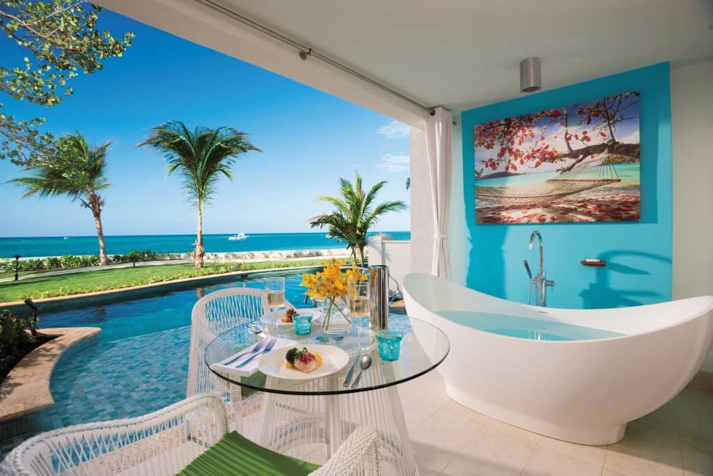 Small seating area next to a tub in a luxury hotel overlooking a pool and an ocean. 