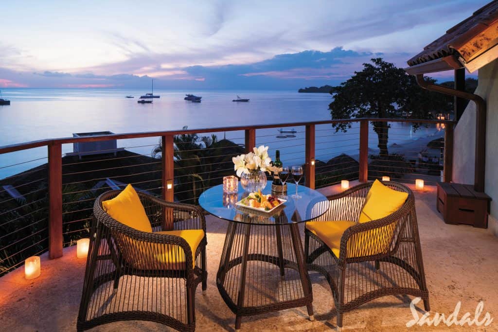 A small glass table with a chair on either side overlooking the water at sunset. 