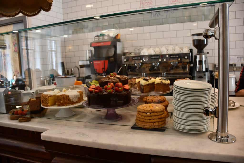 Close up of cakes and cookies behind a glass on a counter.