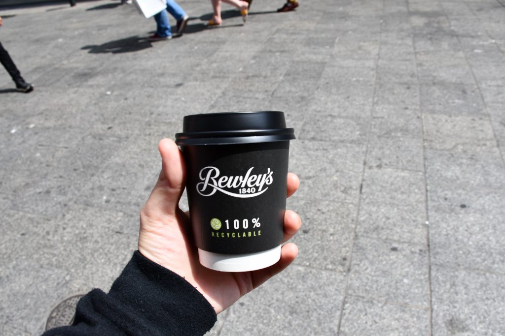 Someone holds a black to-go coffee cup that says Bewley\'s.
