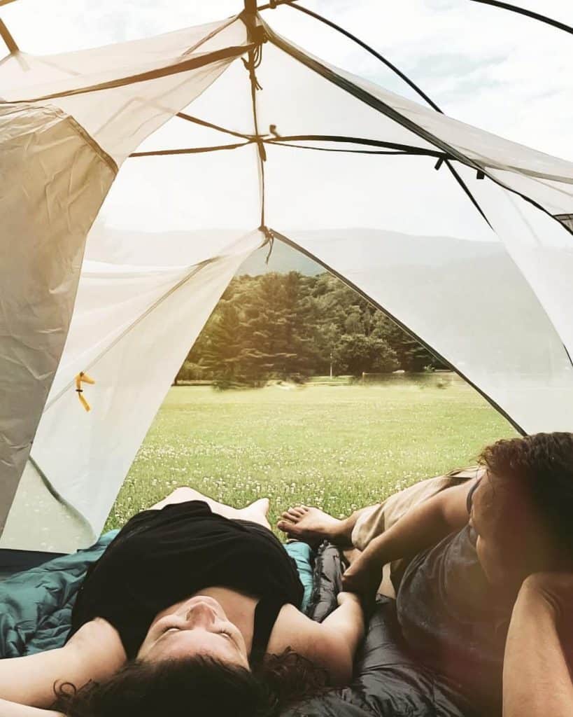 couple laying on sleeping bags inside tent with door open towards field and mountains