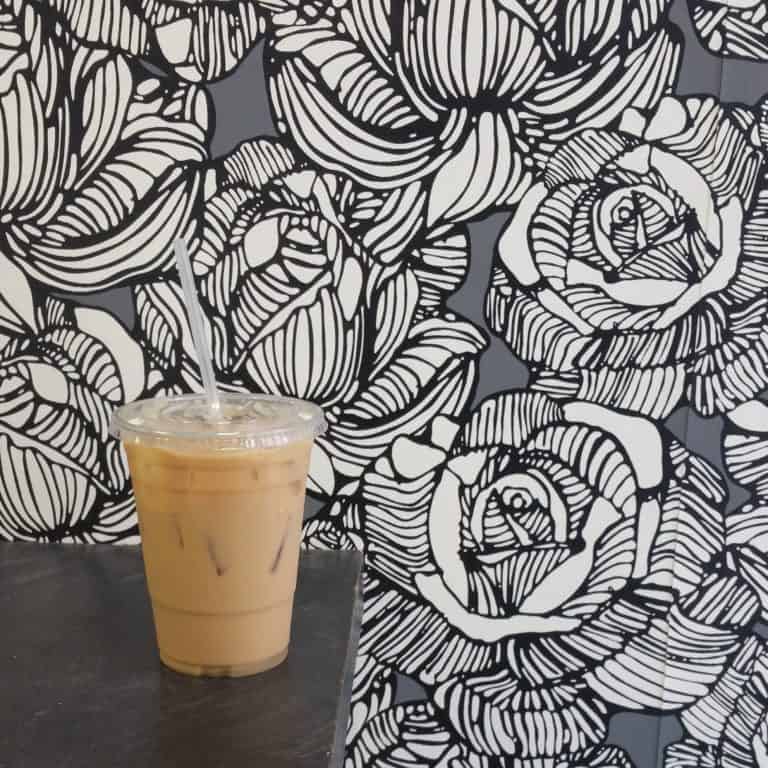 A cup of coffee on a table with black flowers on the wall behind