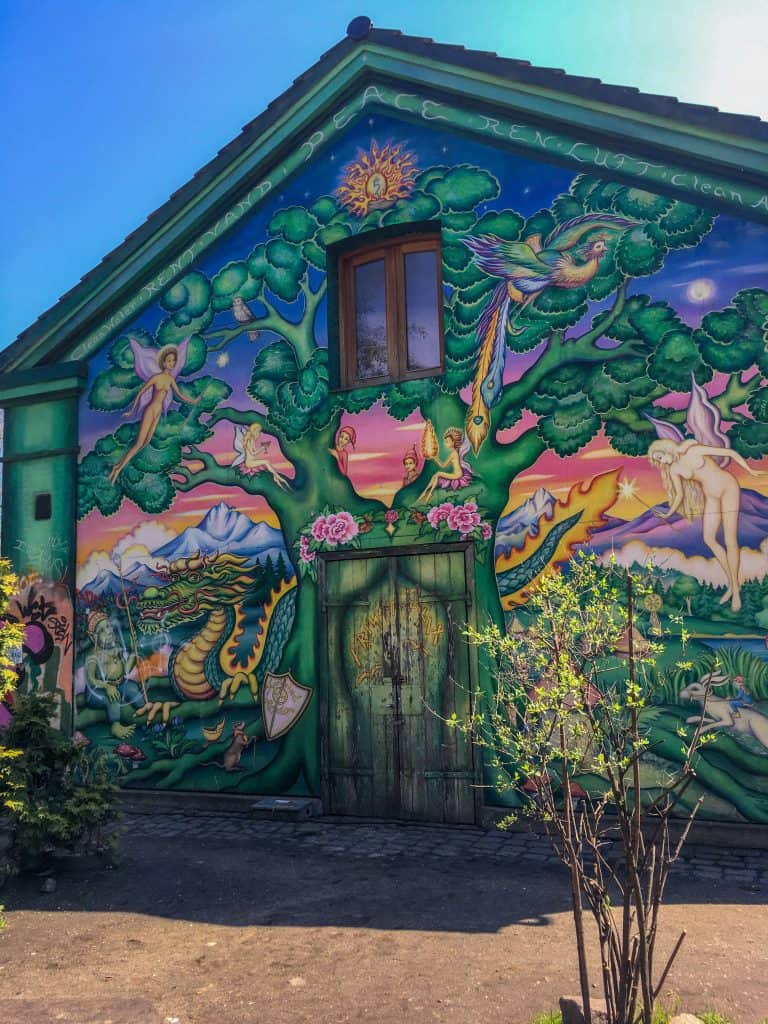 A building painted with street art featuring fairies and green trees.