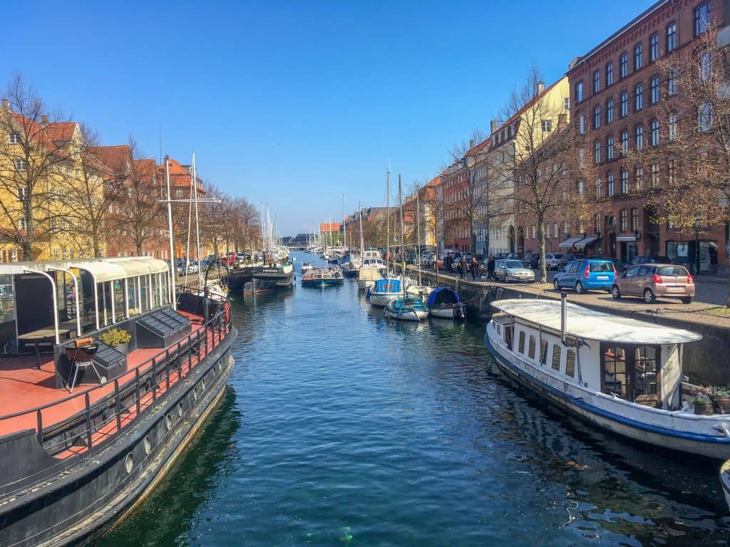 Canal lined with boats. Brick colorful homes are on either side.