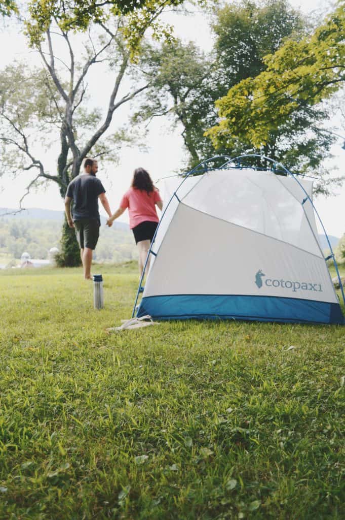 A man and woman hold hands with a tent next to them