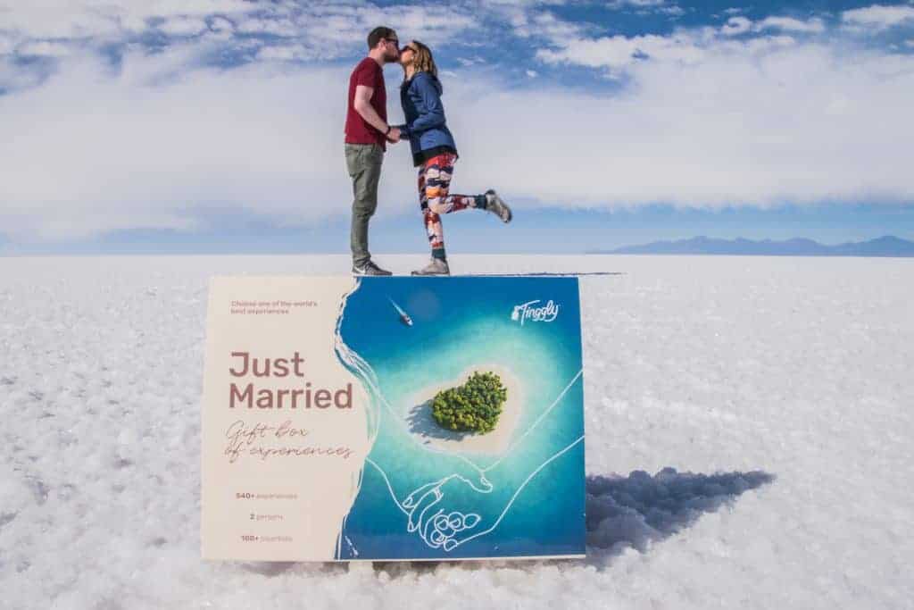 A couple stands kissing on a salt field under a blue sky by a sign that says Just Married.