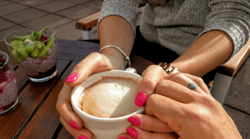 A person holds a cup of coffee while someone else holds their hands.