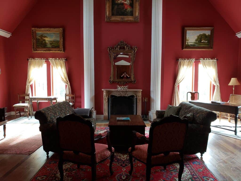 A living area space with red walls is empty next to a fireplace. The walls are lined with old paintings.