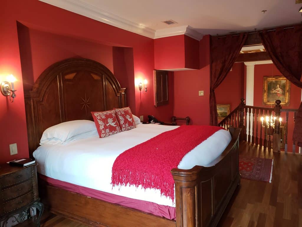 A bed is made with white bedding and red throw pillows. The walls of the room are also red.
