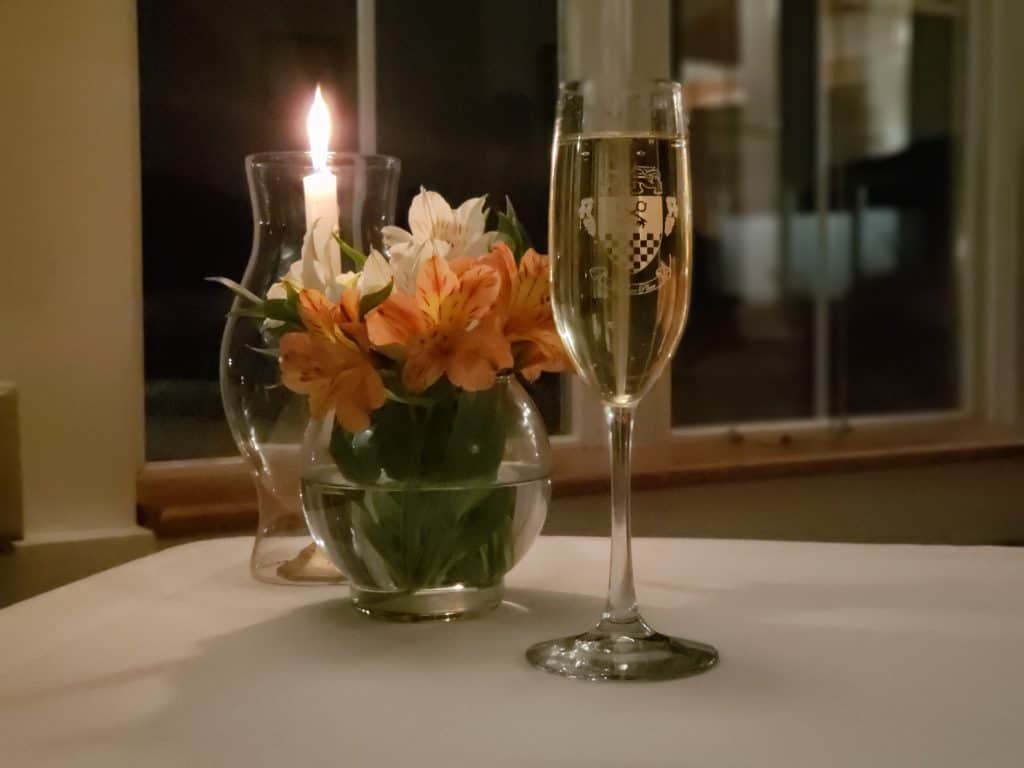 A glass of wine sits on a table next to a vase of flowers and a candle.