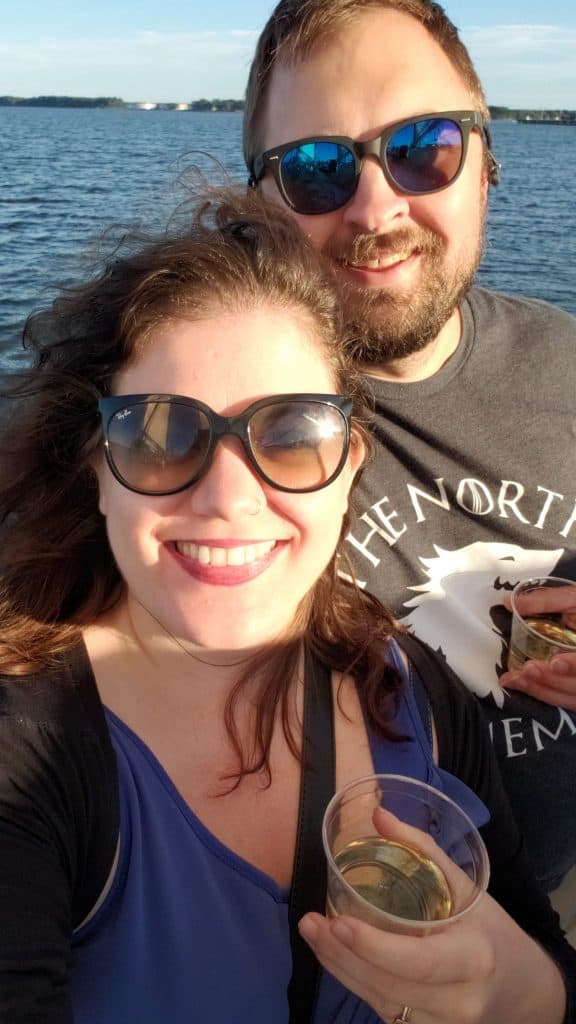 A happy couple takes a selfie on the water while holding alcoholic drinks.