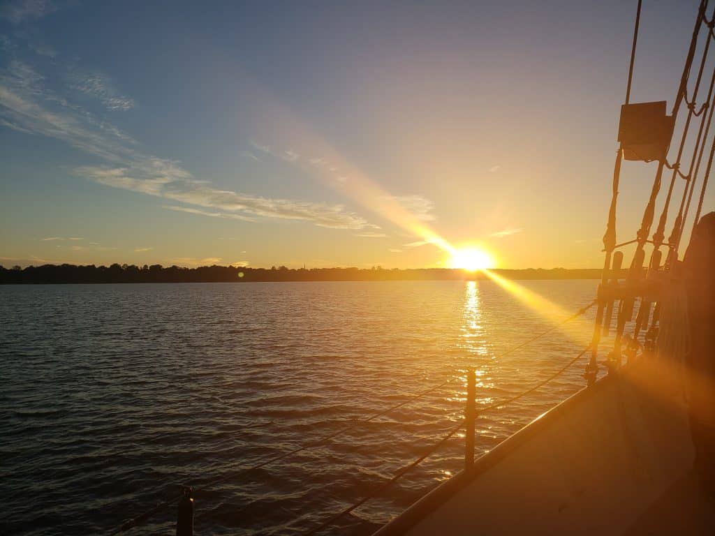 The sun sets over a body of water in the distance from a boat.