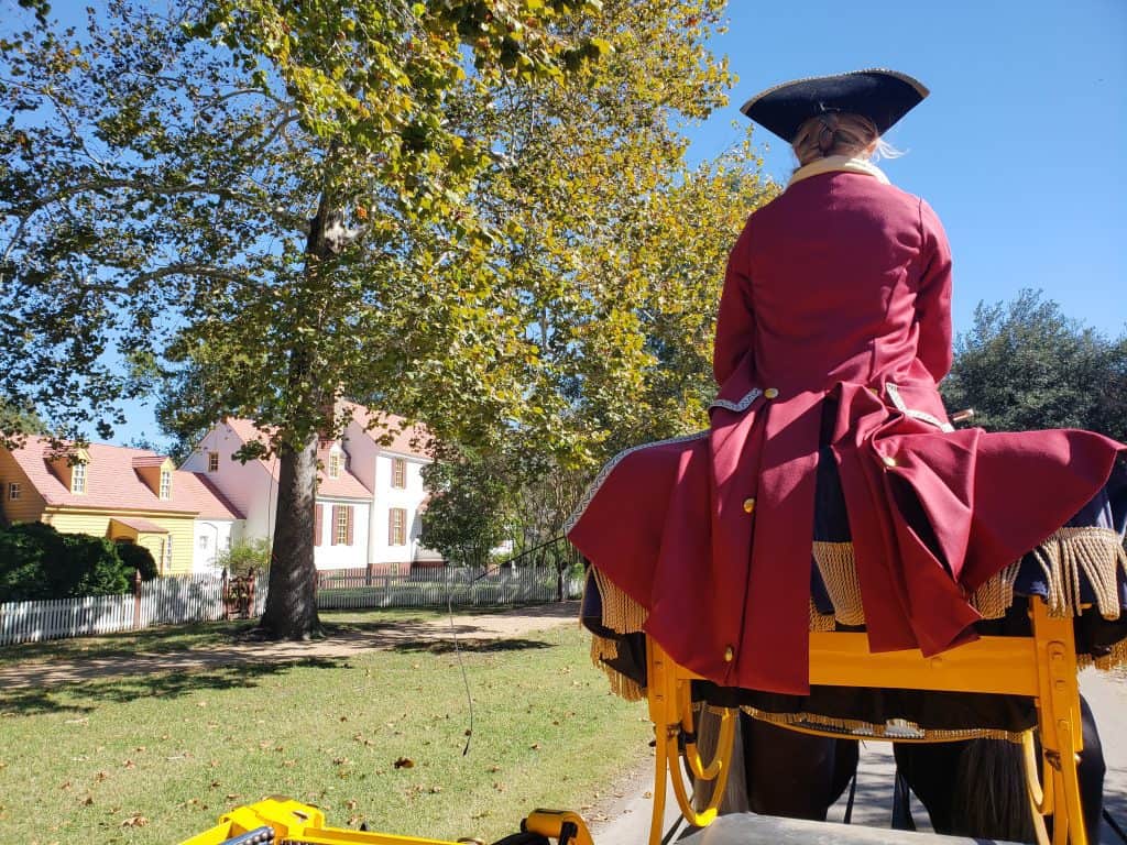 View of a man in a red coat from behind riding a horse-drawn carriage.