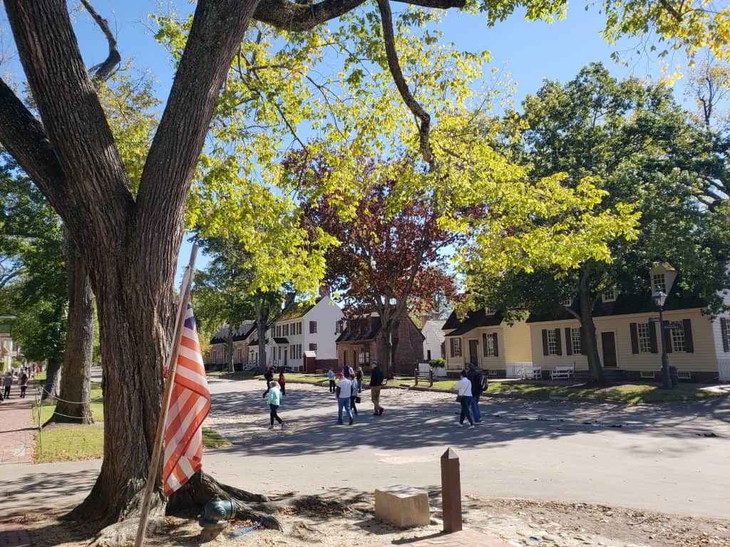 People walk through a historic tourist attractions lined by old buildings and trees.