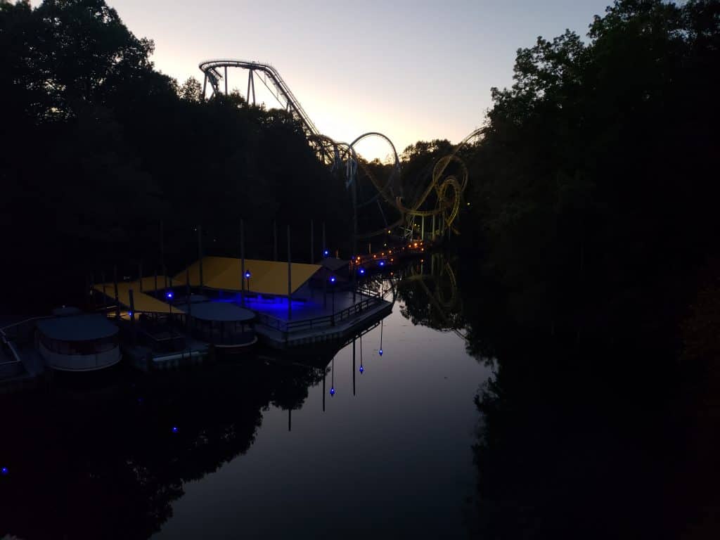 Boats are docked in the water in the evening. A roller coaster is seen in the distance.