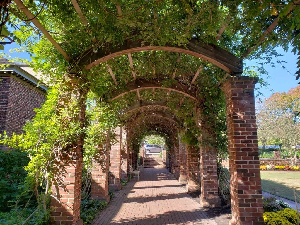 An empty path made of brick is lined by tall brick columns and greenery.