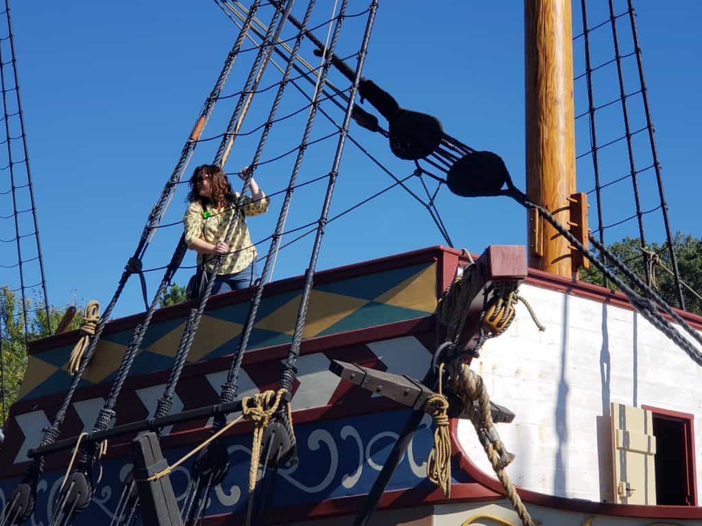 A woman stands on top of a pirate-ship-like building, holding the mast.