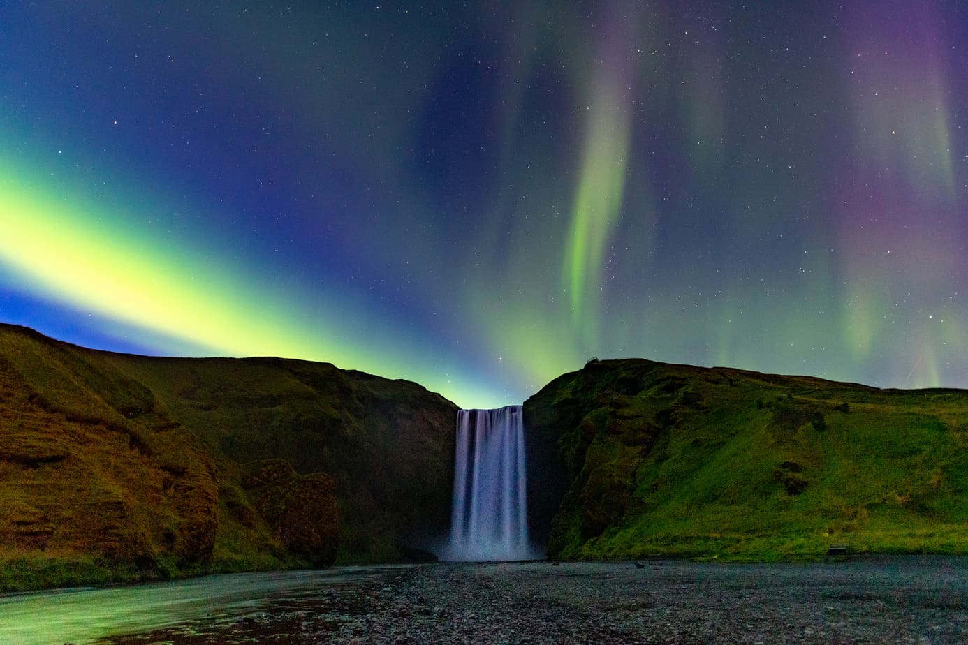 A waterfall cascades down into a pool of water under the Northern Lights.