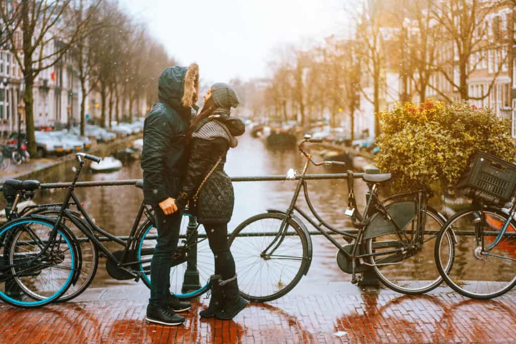 A couple holding hands an about to kiss on a brick bridge over a river. 