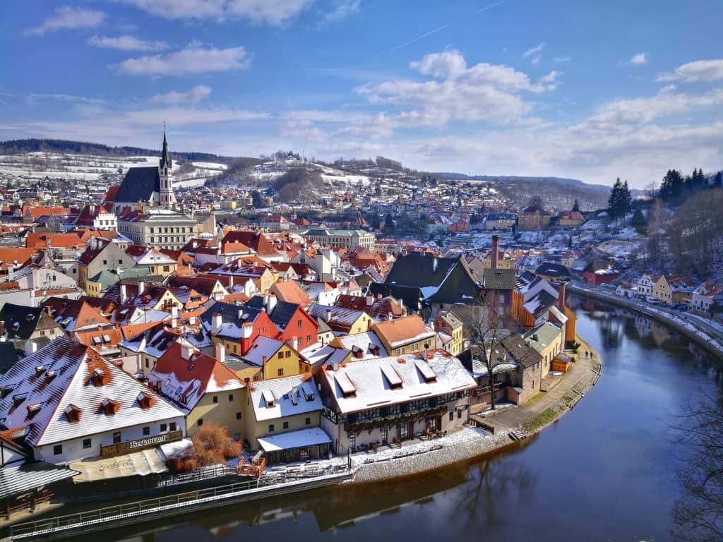 winter in cesky krumlov with snow on the tops of colorful homes along a canal