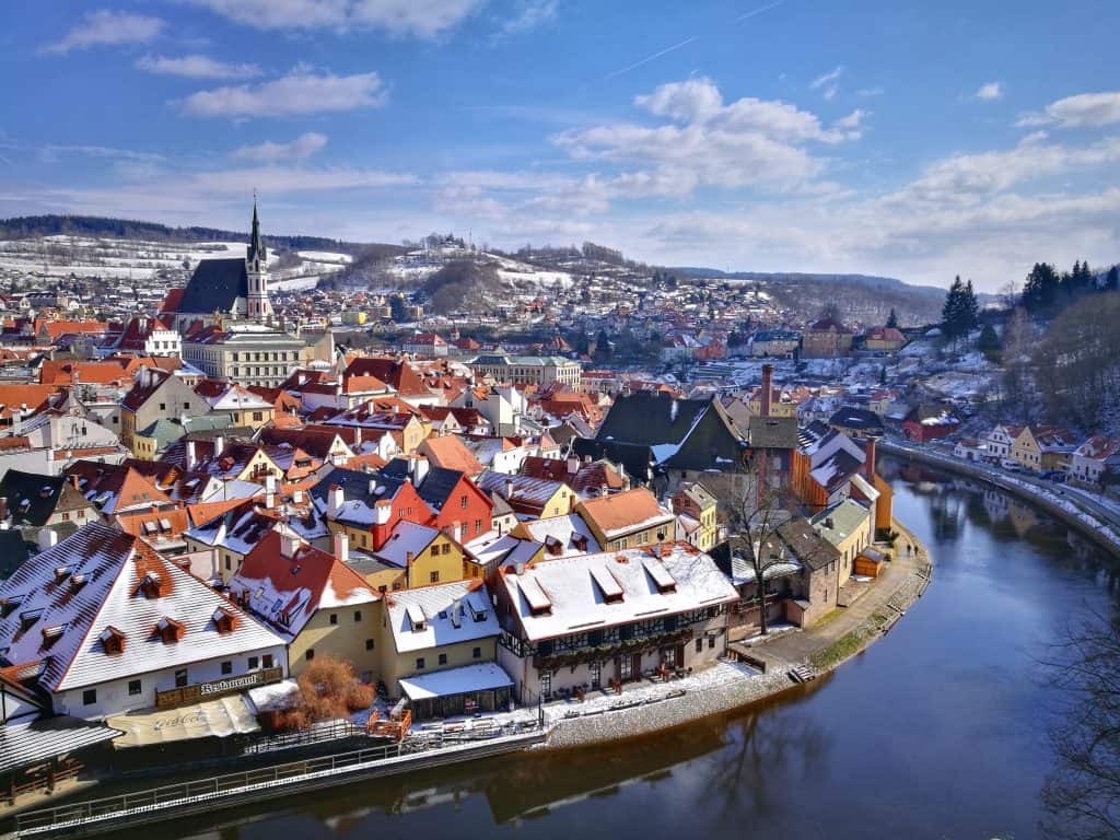 A European city skyline is seen with red roofs in winter, all covered in snow.