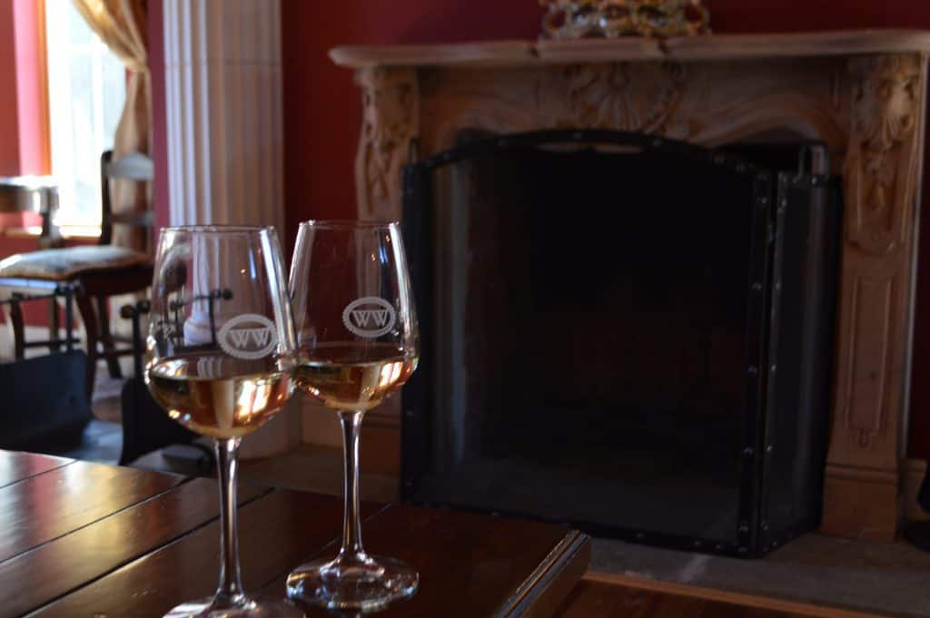 Two glasses of wine on a table with a fireplace behind.